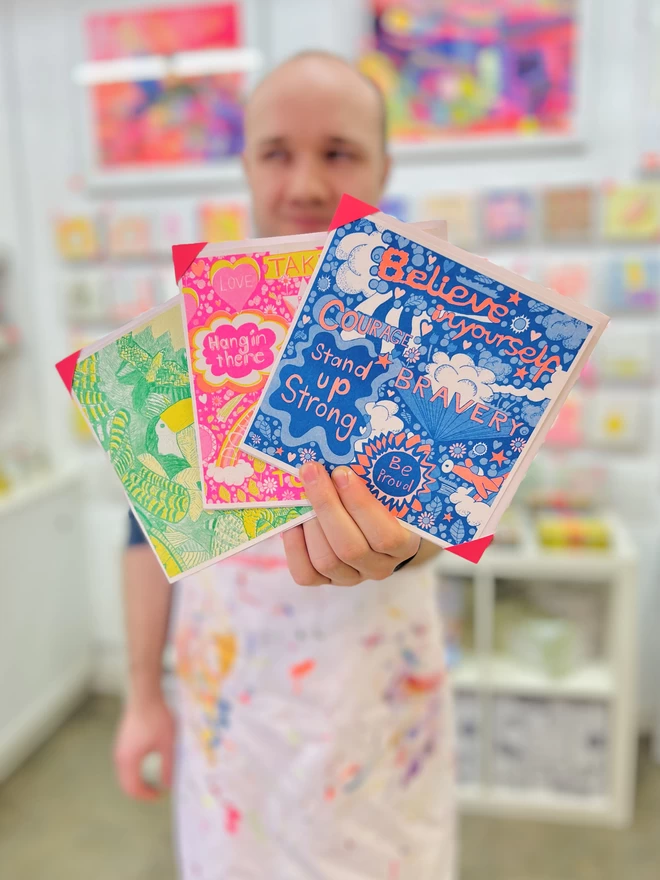 Artist holding a riso printed card called Believe In Yourself with positive affirmations in bright colours