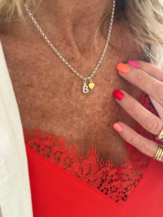 model wears a small silver initial charm sits on a sterling silver chain, with an additional gold heart charm 
