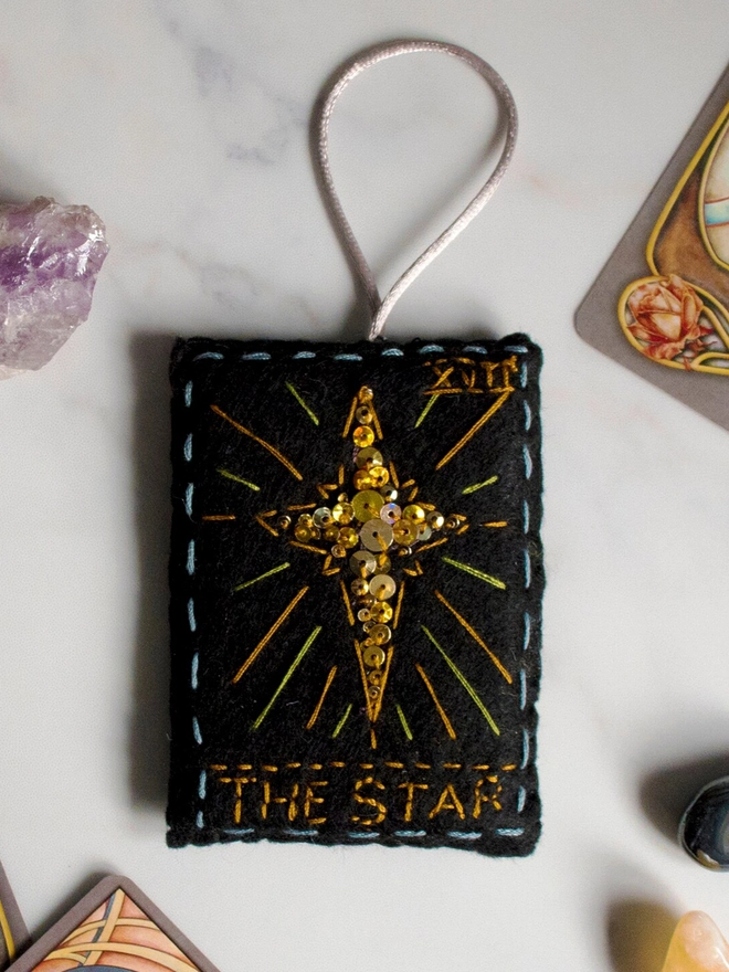 A handcrafted felt ornament with sequins and embroidery depicting "The Star" tarot card. 