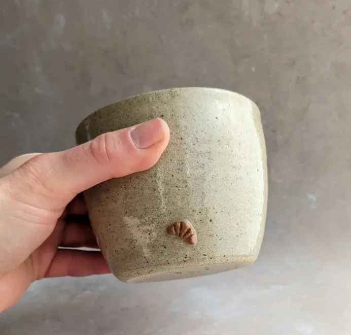 Biscuit colored croissant coffee cup with a subtle croissant design, placed against a grey marble background.