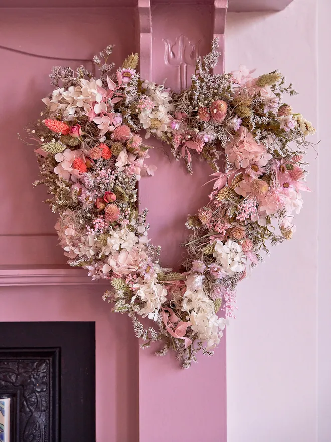 Spring coloured wreath in pinks, whites and creams hanging on a pink mantlepiece