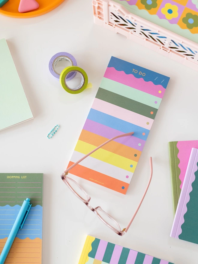 Rainbow tear off 'To Do' list pad sits on table with a pair of reading glasses and other colourful stationery items from the Raspberry Blossom Happiness stationery collection