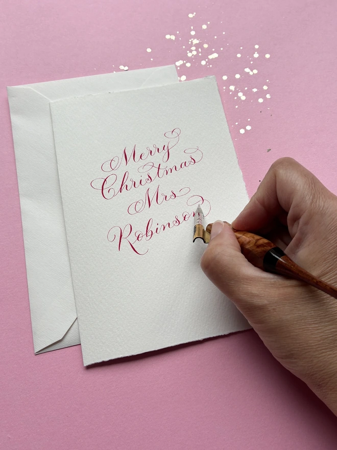 Hand holding a calligraphy pen writing a Christmas card