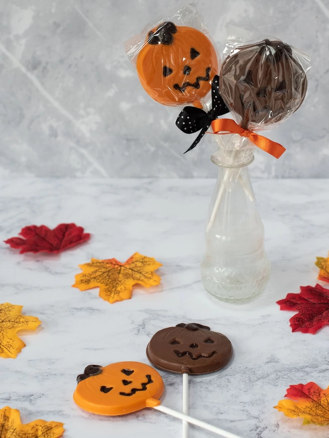 Orange and milk chocolate pumpkin lollipops surrounded by leaves