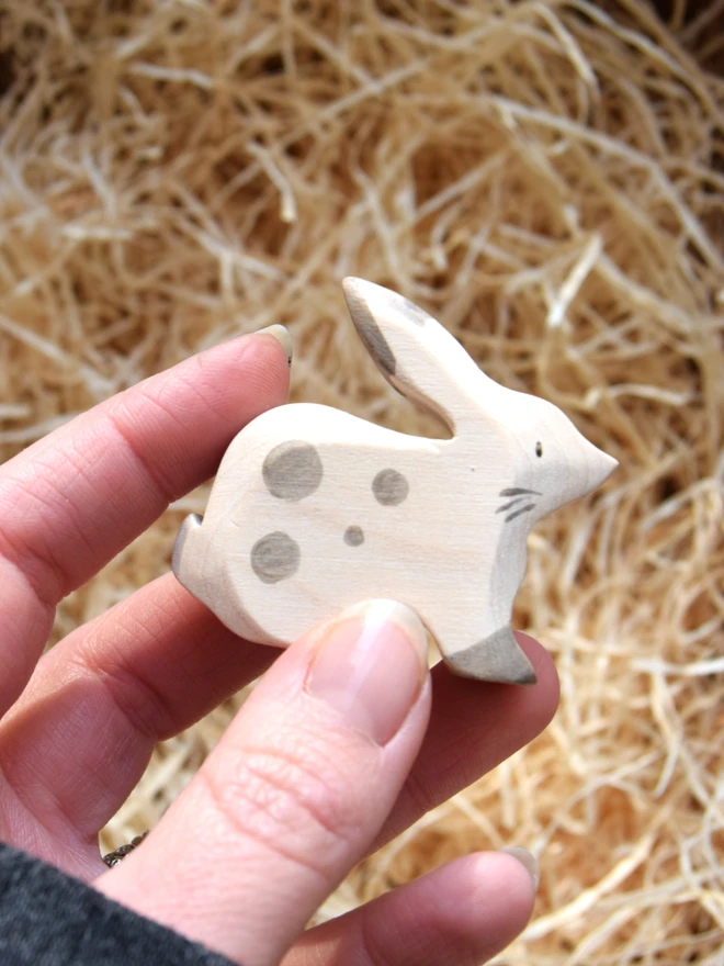 wooden spotty white bunny being held above woodwool