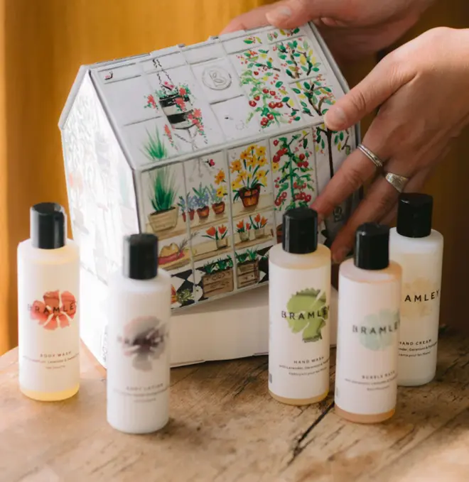 cardboard box in the shape of a greenhouse, with illustrated design, next to five bottles of product with white lables and black lids