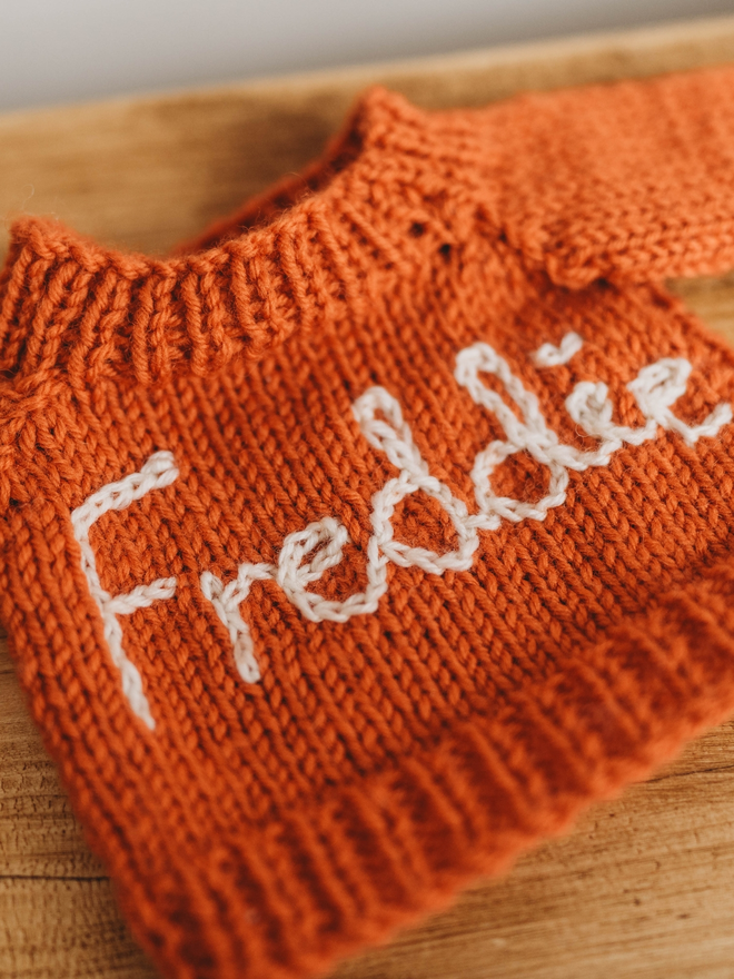 hand knit orange personalised teddy bear jumper on wooden shelf