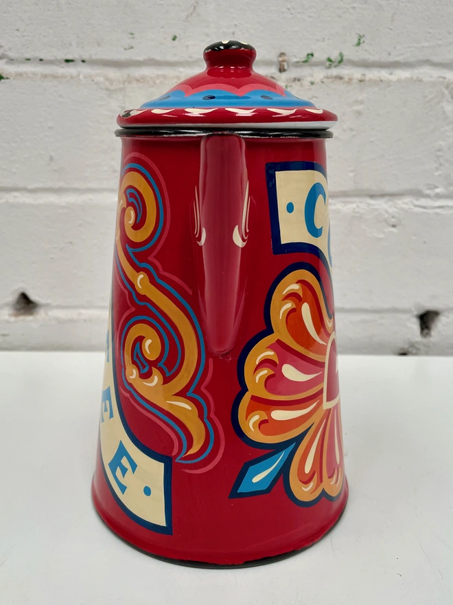 Red vintage coffee pot, hand painted with a fairground inspired design in pink, orange and yellow. 'Coffee' is painted in a banner through the centre of the design.