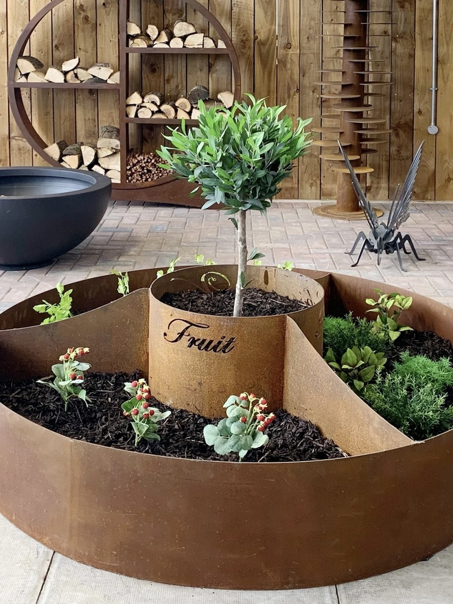 Circle Of Life Corten Vegetable Planter, in room with plants growing in soil. 