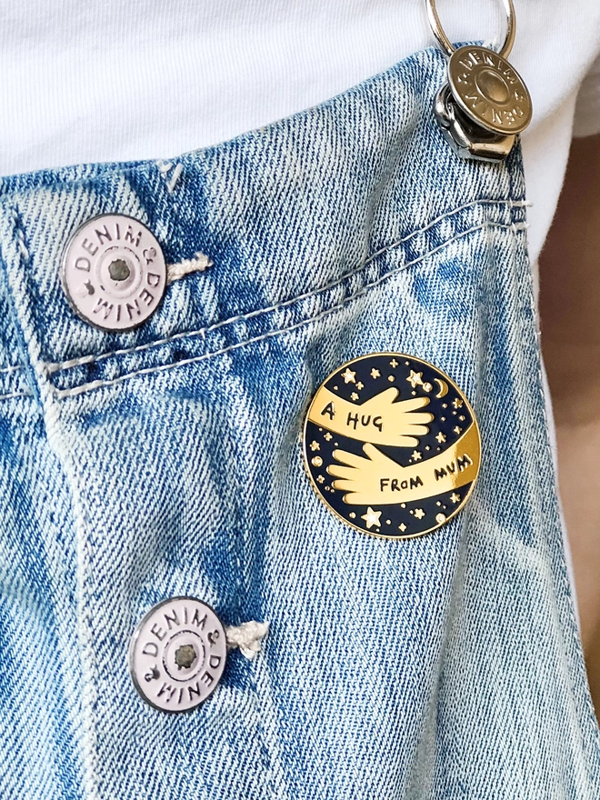Child wearing dungarees with A Hug From Mum Navy blue and gold pin badge attached.