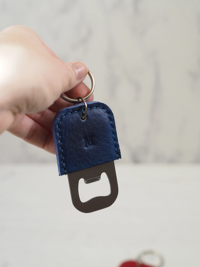 Handmade personalised leather bottle opener. A dark blue leather key ring with bottle opener function, stamped with a letter in the middle of the leather