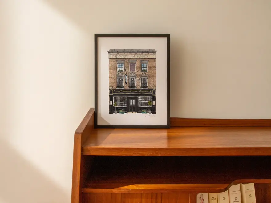 Wapping Prospect of Whitby Giclée Print (Unframed), a print of a pub sitting in a frame on a wooden shelf against a plain backdrop. 
