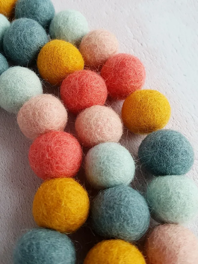 A felt ball garland in coral, mustard, duck egg, mint and peach colours.