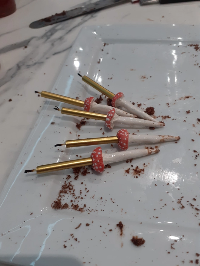 Five reusable handmade ceramic toadstool and mushroom cake candle holders with gold candles, shown after use on a white serving platter.