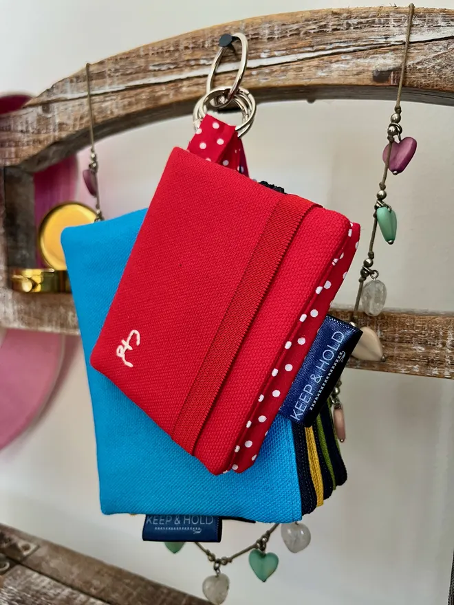 Red Card Wallet with keyring hanging with a set of colourful coin purses. Card wallet is embroidered with a £ sign in white thread.