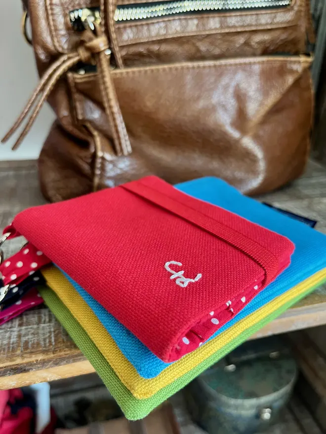 Stack of colourful coin purses with a smaller red card wallet on top. Leather handbag in the background.