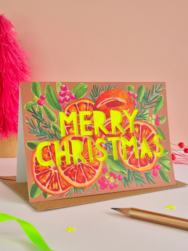 Christmas Card with blood oranges illustration, paper cut text that says Merry Christmas and a neon yellow backing paper 