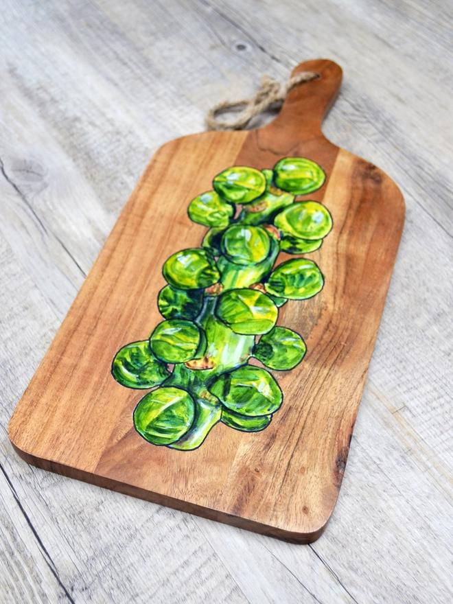 A wooden serving board with a handpainted design of Brussels sprouts