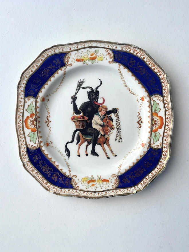 a naughty Christmas Krampus stealing a child, the image is victorian and is printed directly onto an ornate vintage plate