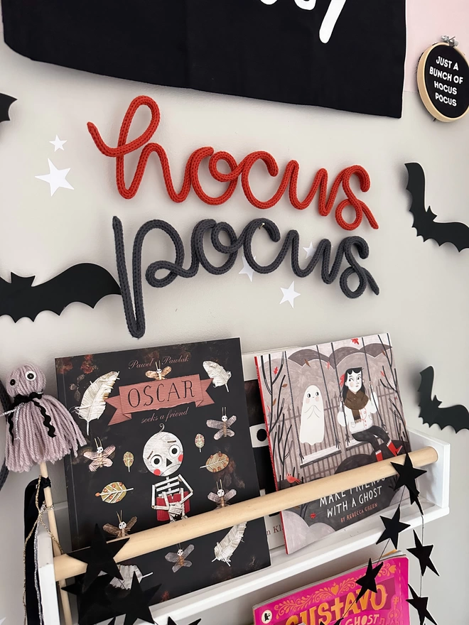 Knitted Halloween Phrase - 'Hocus Pocus', Hanging up in a kid's bedroom above some Halloween books with paper bats decorating the wall. 