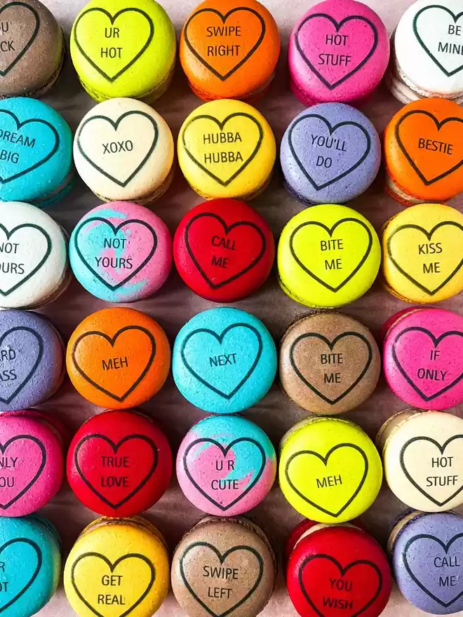 Colourful macarons decorated like conversation love heart candy in a row on a pink background