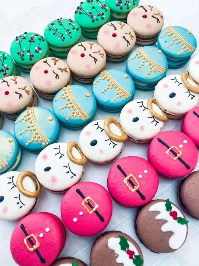 several decorated macarons themed like Christmas character - fairy lights, rudolf the red nosed reindeer, Christmas bauble, angel, Santa and Christmas pudding are arranged on a table