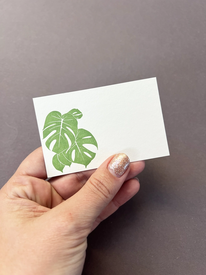Single Green Monstera leaf letterpress card held in a woman's hand to show scale