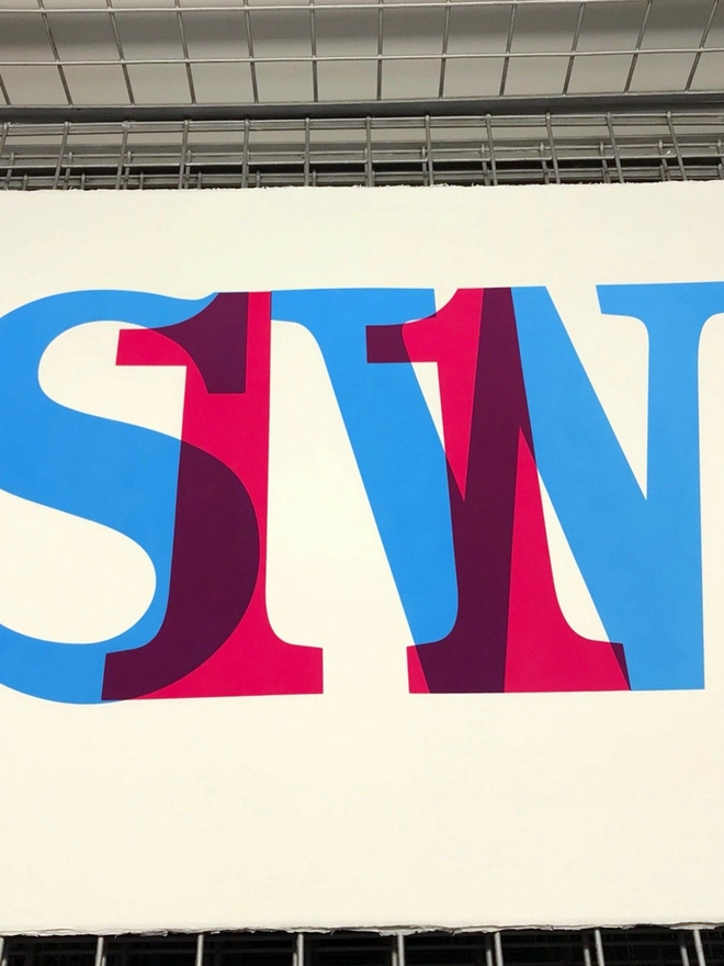 On the drying rack from above, showing a screenprint of SW11, overlapping magenta and cyan blue.