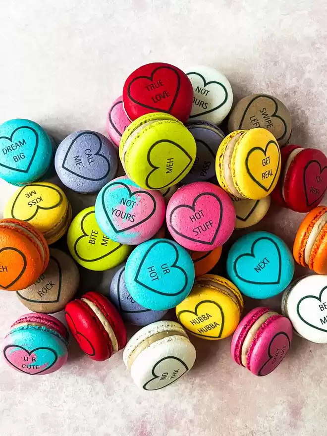 a pile of colourful macarons with hearts drawn on them