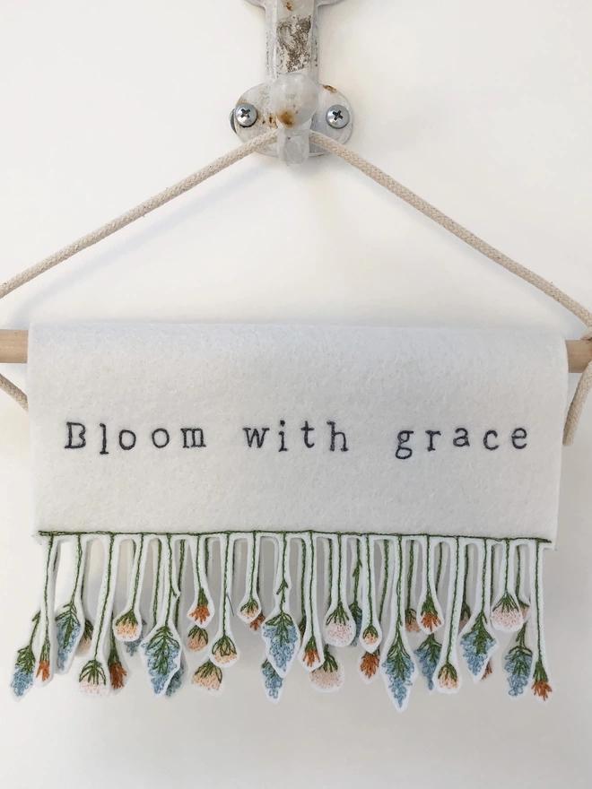 shes a wildflower banner with phrase bloom with grace on a hook