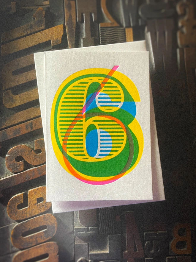 Handmade letterpress 6th birthday card featuring bold overlapping numerals printed in vibrant fluorescent cyan, magenta and yellow inks. Each card is individually hand printed using traditional letterpress techniques on luxury paper stock, creating a beautifully tactile finish with a deep impression and rich layered colours inspired by the CMYK printing process. Printed on a traditional letterpress from 1915.