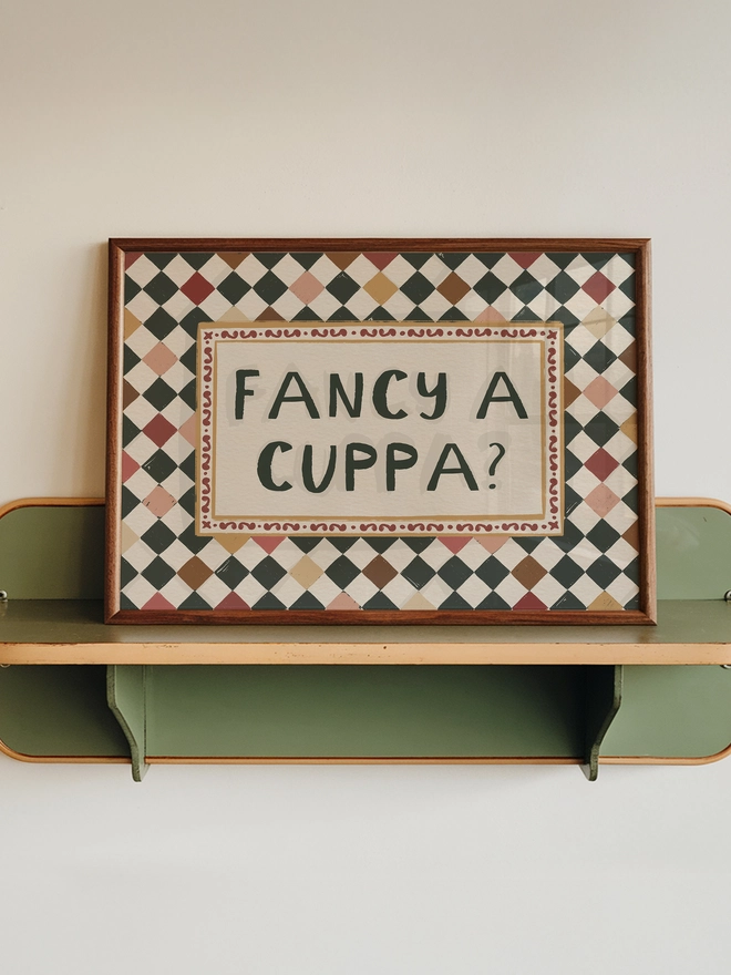 Checkerboard frame with jammy biscuit colour squares with central text ' fancy a cuppa' 