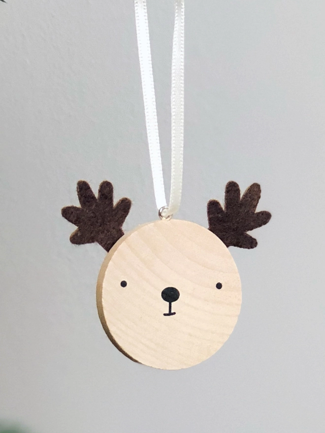 A small wooden and felt reindeer decoration hangs on a Christmas tree branch.