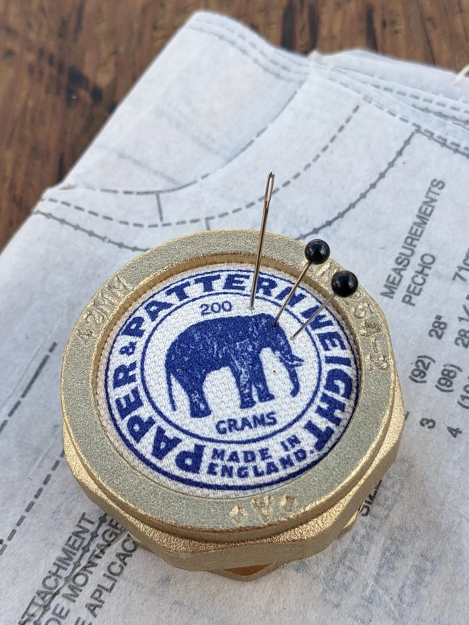 Blue elephant brass pattern & paper weight with needle and pins lying on a sewing pattern