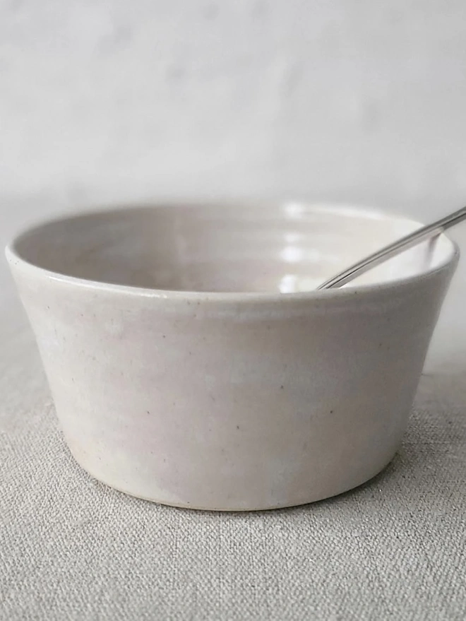 Classic Ceramic Breakfast Bowl, a breakfast bowl sitting on a grey carpet against a plain backdrop. It is accompanied by a spoon. 