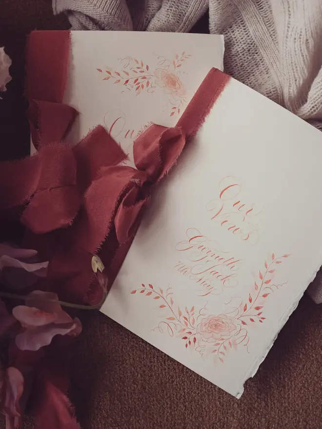 personalised calligraphy wedding vow booklet. white booklet with rust red calligraphy on cover.