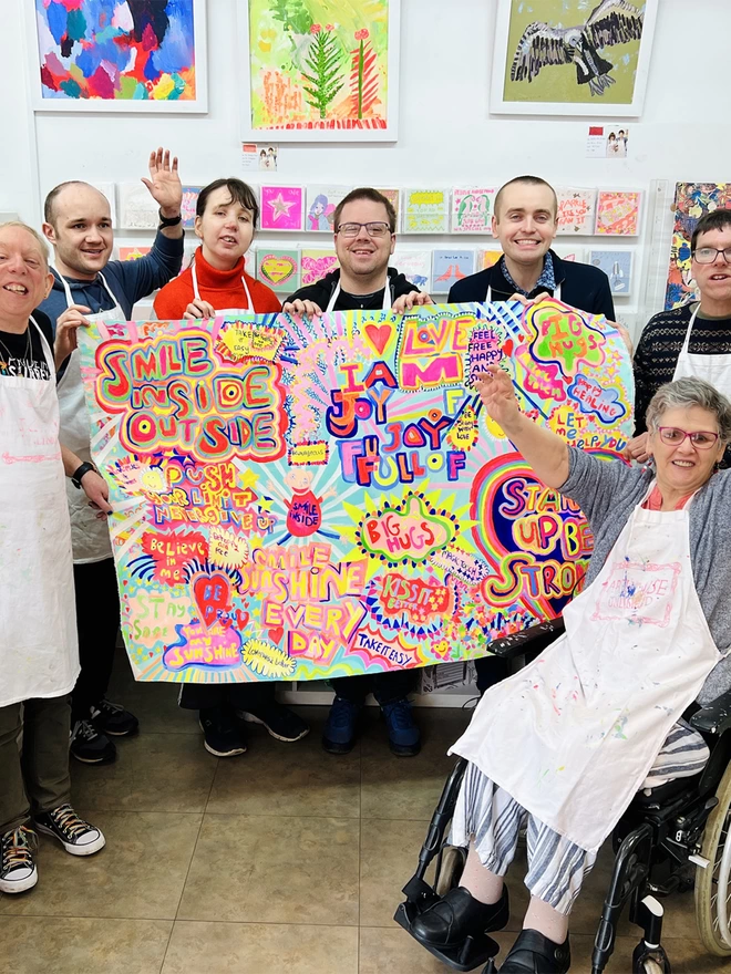 7 artists holding colourful original artwork for full of joy 100% organic cotton charity tea towel