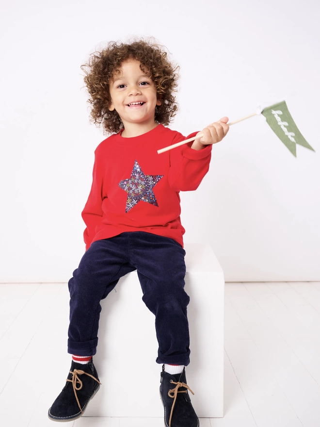 A little boy wearing a red tee with a Liberty star print star sewn on the front