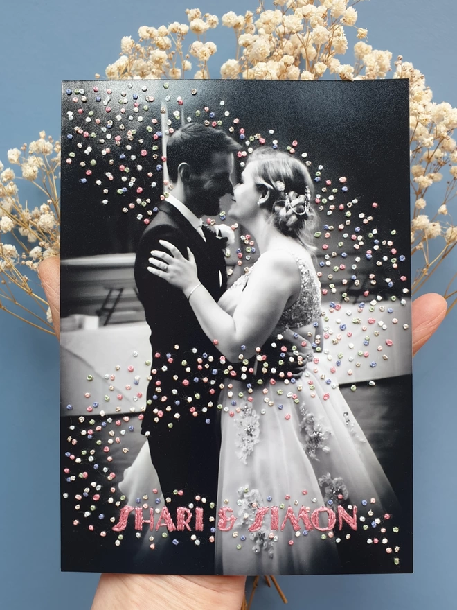 Wedding photo in B&W with hand embroidered confetti swirling around them and name across the bottom