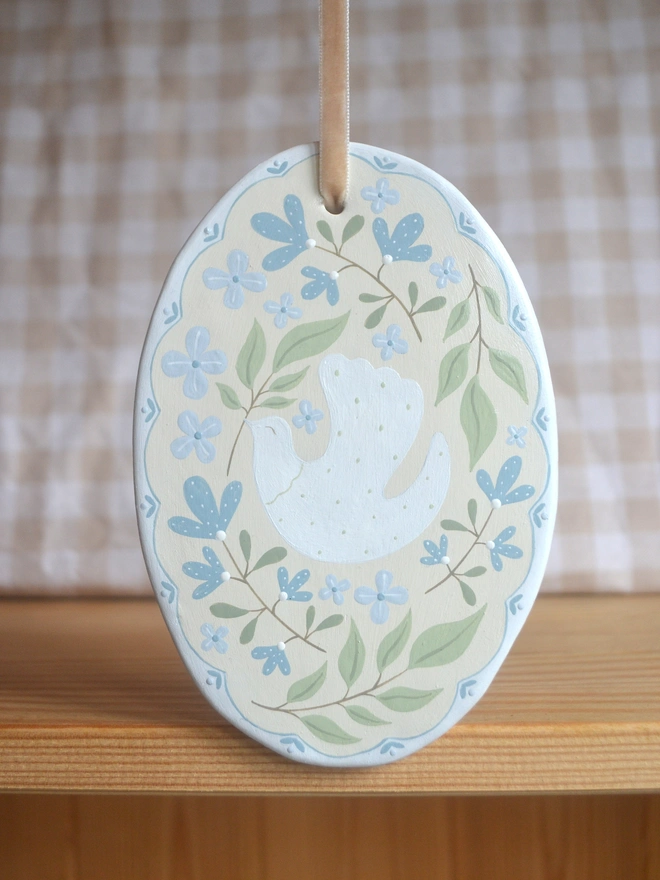 oval ceramic decoration with white dove illustration and blue and green floral decor