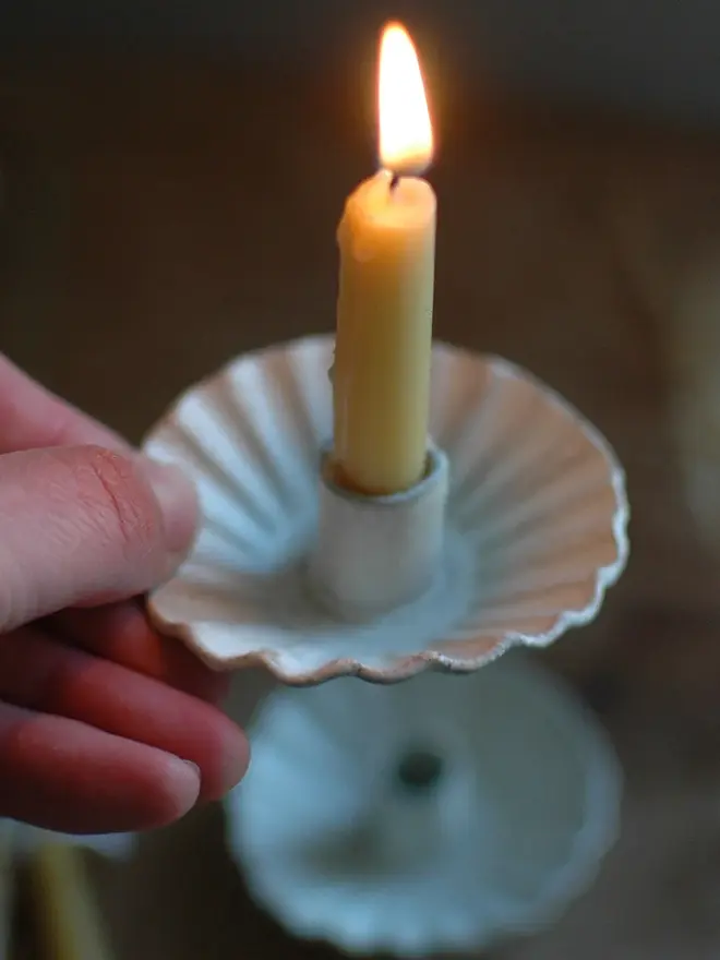 Handmade White Ceramic Candlestick Holder, a white candle holders on a wooden surface. It is accompanied by a lit candles. 