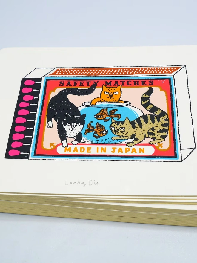 Three Cats And Two Fish Matchbox Lucky Dip, a colourful matchbox design in the centre of a white screenprint. 