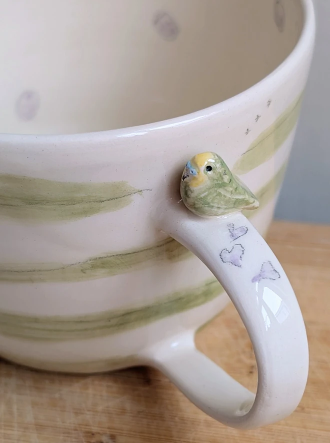 green budgie cup with tiny bird on the handle green stripes and lilac spots