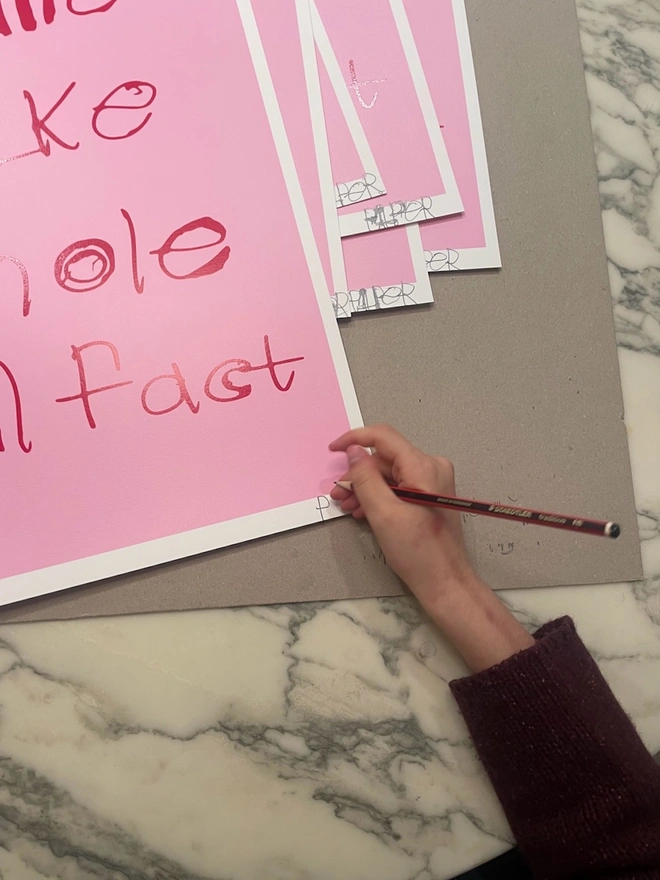 The corner of the pink screen print with red writing and you can see pipers hand signing 6 of her screenprints