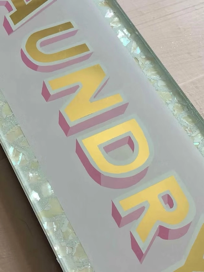 'Laundry' Glass And Gold Leaf Sign, a gold and glass sign sitting on a plain surface. 