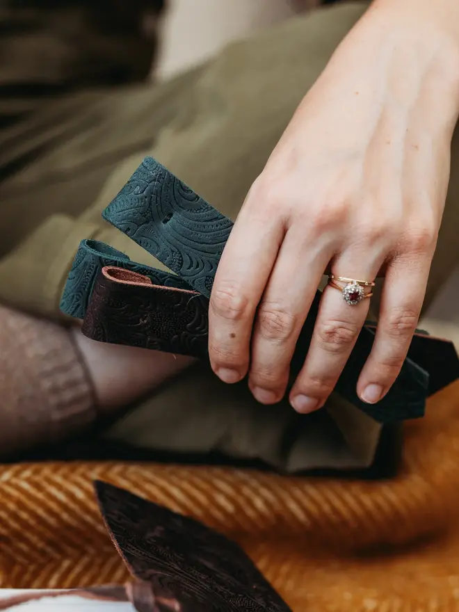 botanical leather bookmark. a selection of green and red book marks  held in hand against a rust coloured rug.