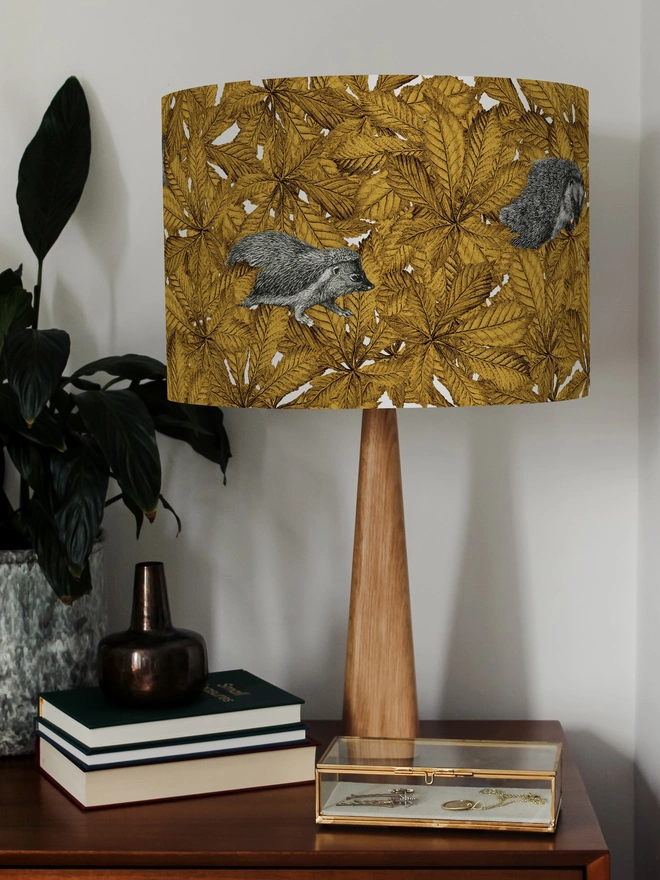 Handmade lampshade featuring cosy hedgehogs nestled among autumnal yellow leaves, creating a warm and whimsical woodland design.
