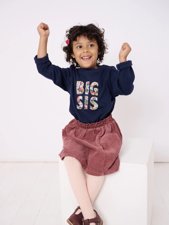 big sis appliquéd on a long sleeve navy cotton t-shirt worn by a happy little girl