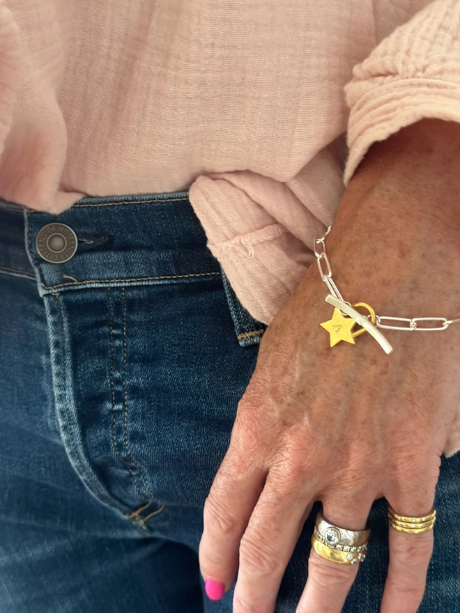 model wears a chunky gold star charm on silver paperclip bracelet with T bar fastener