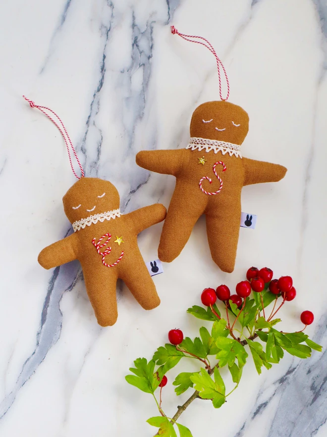 Brown linen gingerbread man christmas tree ornament with a letter hand embroidered in candy cane colours, star shaped sequin, crochet cotton lace around the neck, smile embroidered in white and candy cane colour string to hang. 